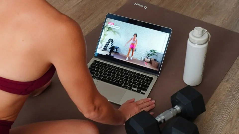 A Born to Sweat workout playing on a laptop next to dumbbells